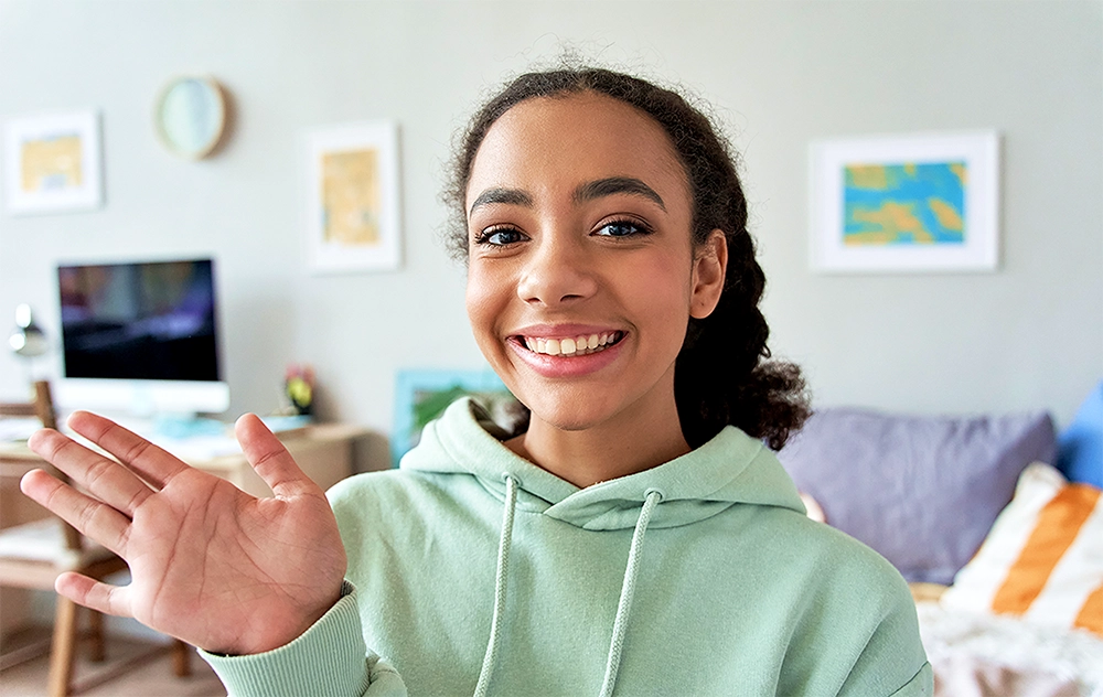 Smiling teen waving during a video call.